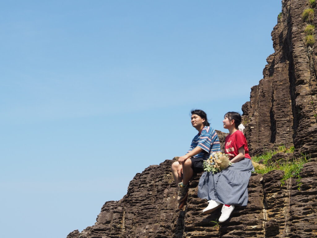 青空の下、岩に並んで座る店長のりょうとさんとスタッフのななさん
